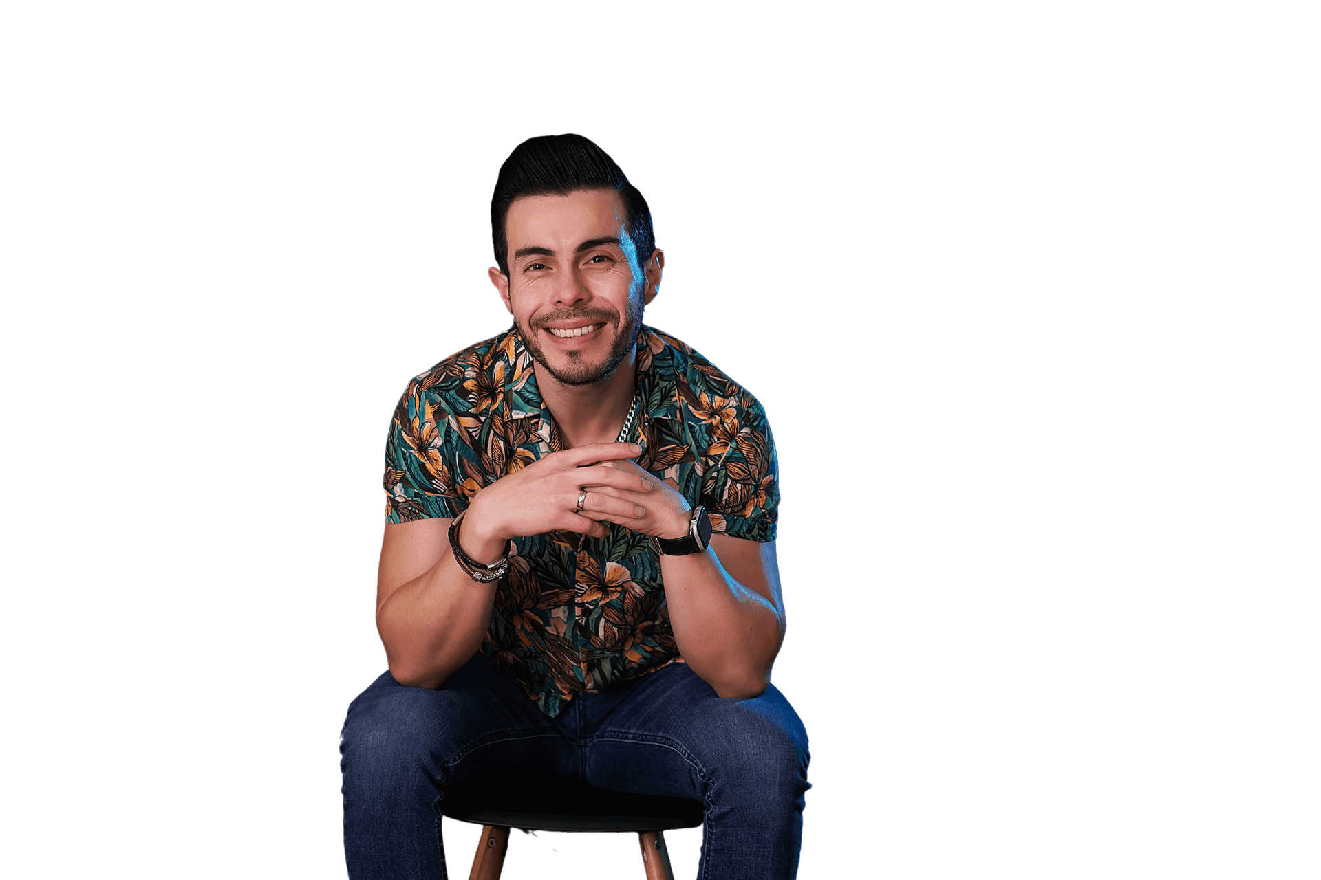 Person sitting on a stool wearing a floral print shirt and jeans with hands clasped together.